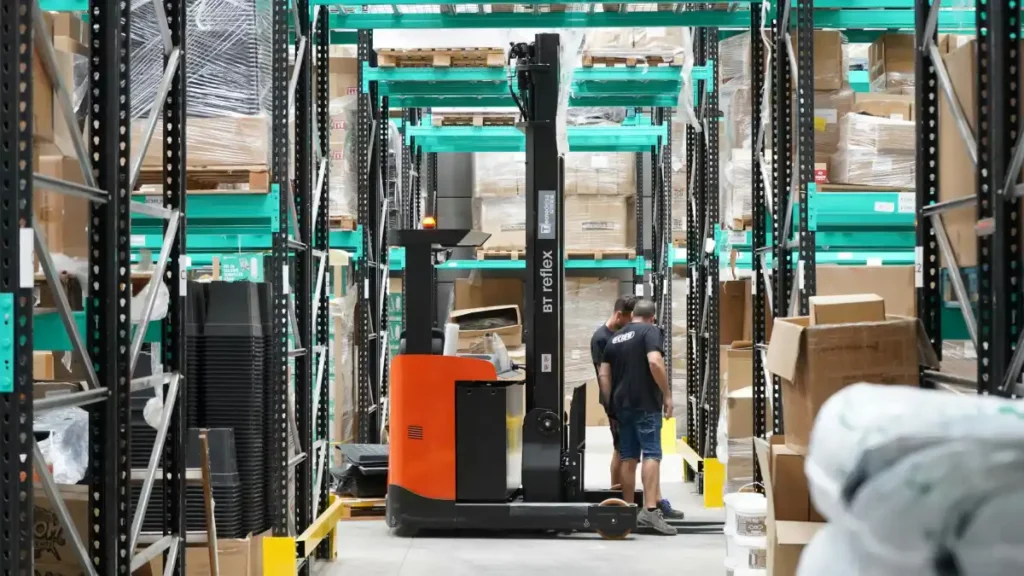 Pekerja dan forklift di dalam gudang logistik yang besar dengan rak-rak tinggi